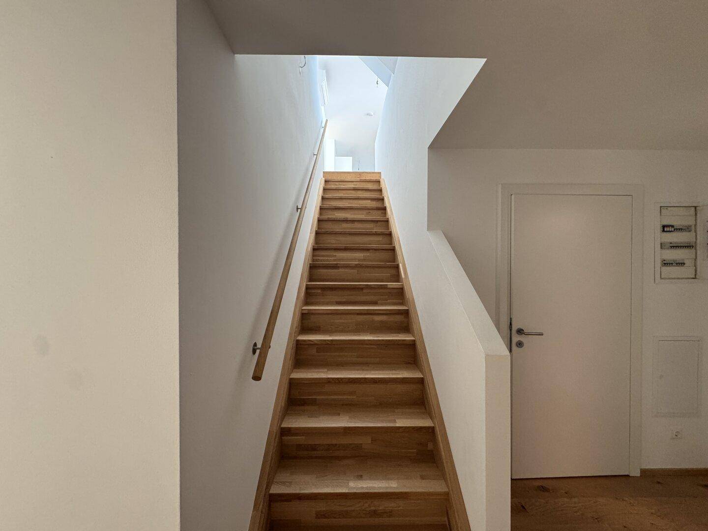 Moderne Holztreppe mit schlichtem Handlauf, die die beiden Ebenen der Maisonette verbindet.