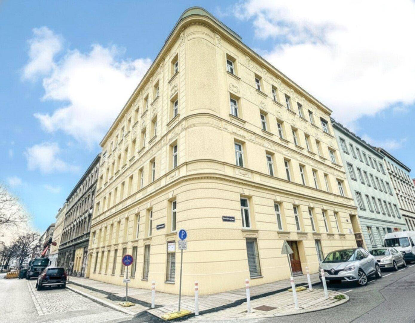 Eckgebäude mit gelber Fassade an einer städtischen Straße unter blauem Himmel.