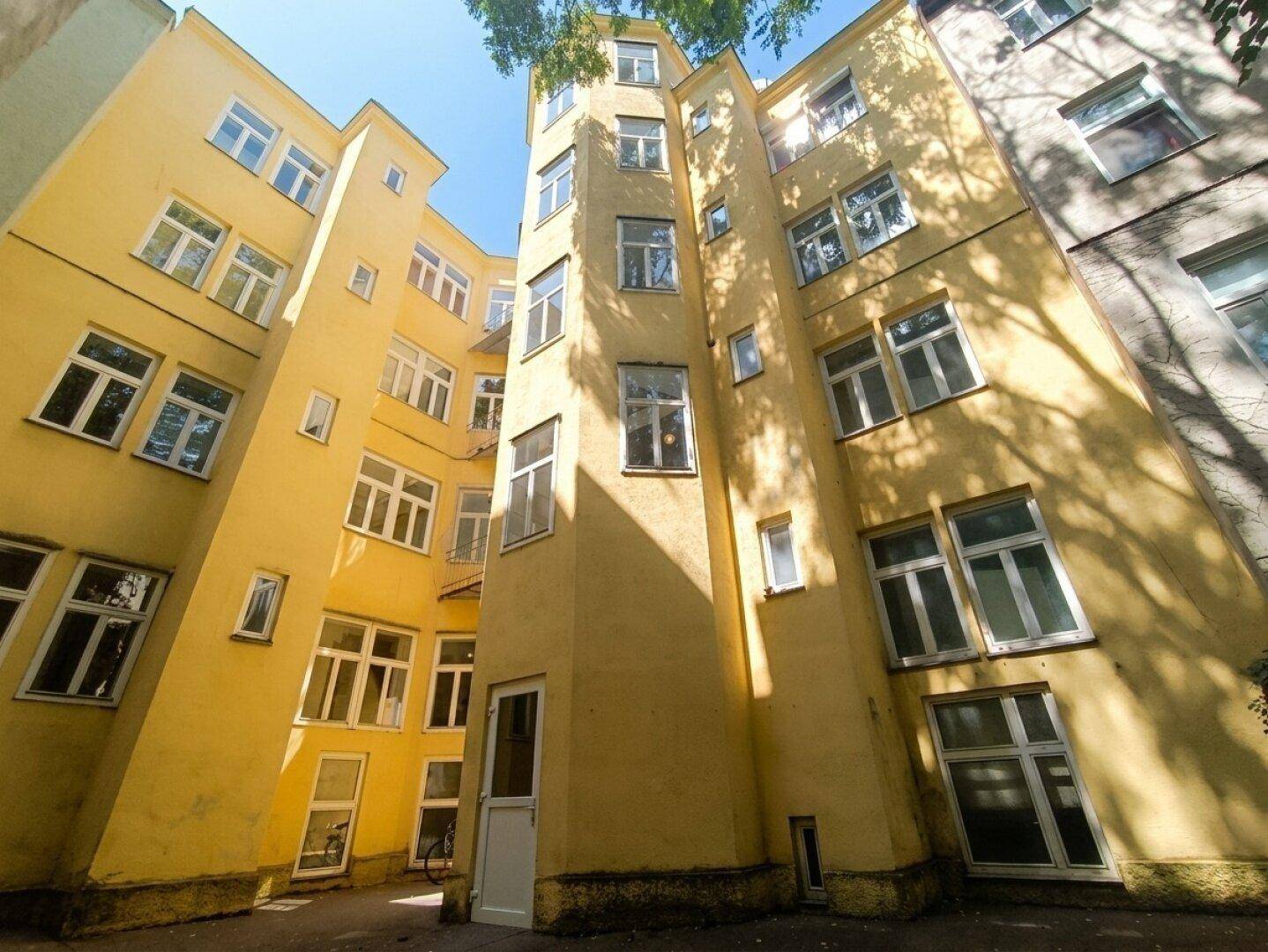 Heller Innenhof eines Gebäudes mit gelber Fassade und vielen Fenstern.