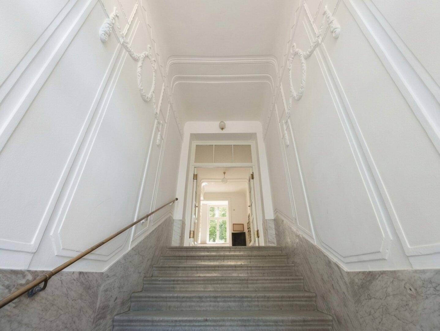 Eindrucksvolles Treppenhaus mit Marmorstufen, Stuckverzierungen und hohen Decken.