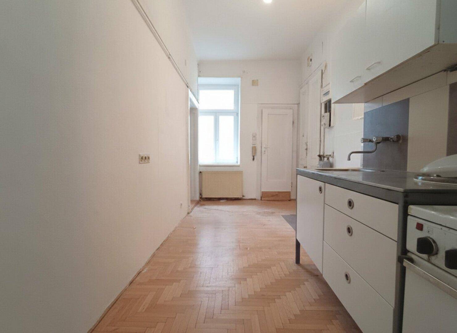 Einfache Küche mit älteren Einbauschränken, Spüle und Fischgrätparkettboden.