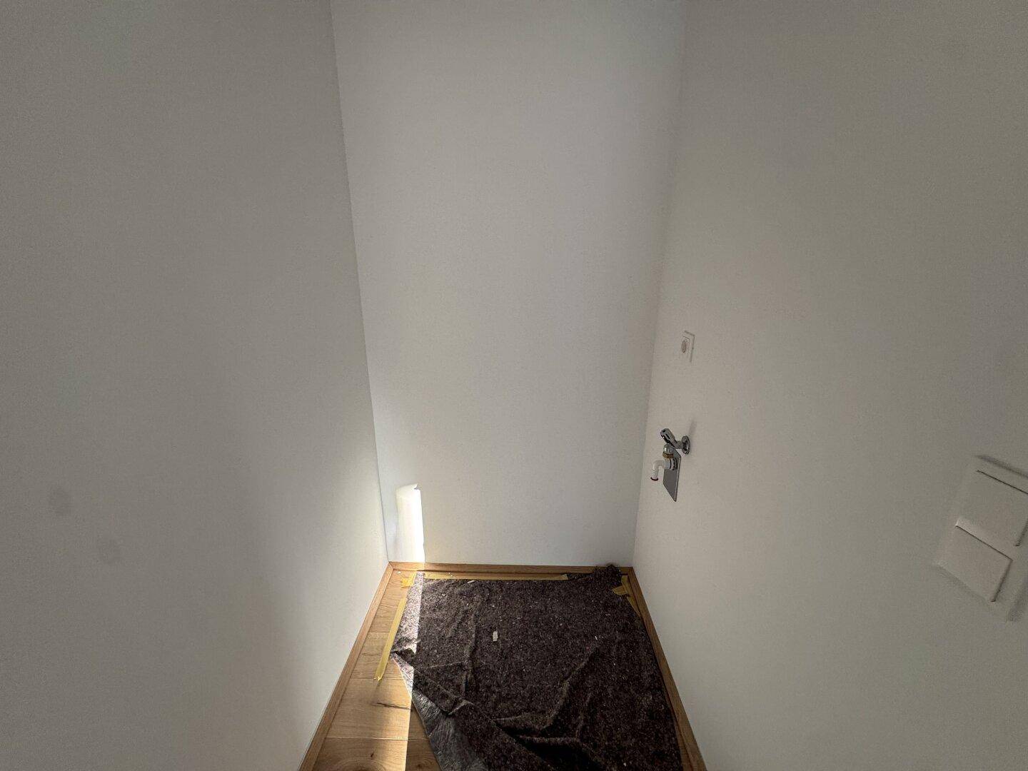 Kleiner Hauswirtschaftsraum mit Holzboden und Anschlüssen für Waschmaschine oder Spüle.