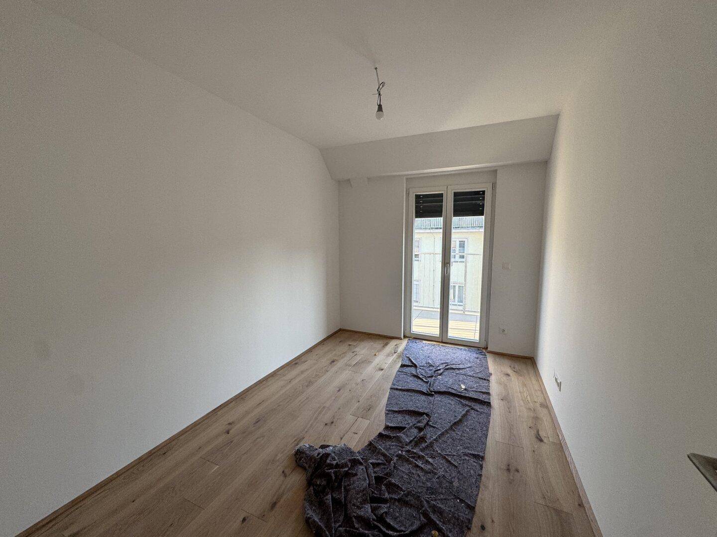 Helles Schlafzimmer mit Holzboden und Zugang zu einem französischen Balkon.