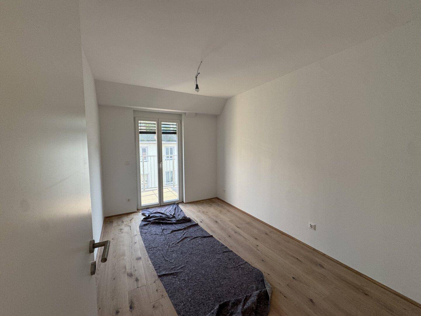 Geräumiges Schlafzimmer mit Holzboden und Fensterfront zum französischen Balkon.