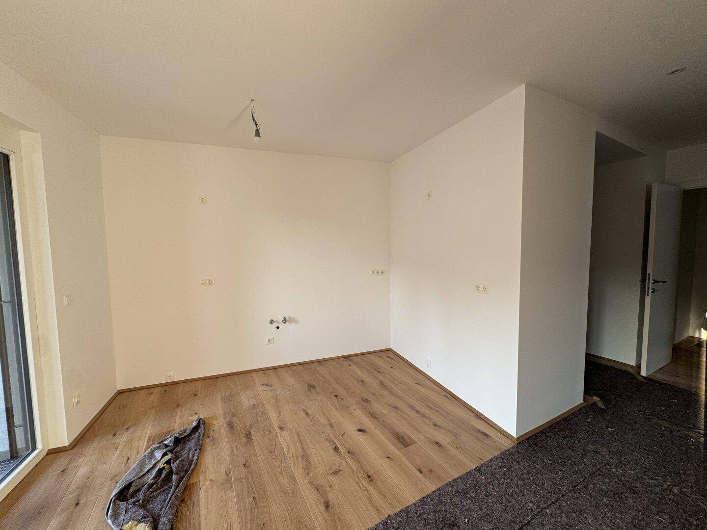 Leeres Zimmer mit Holzboden und Fenster, bereit für die individuelle Gestaltung.
