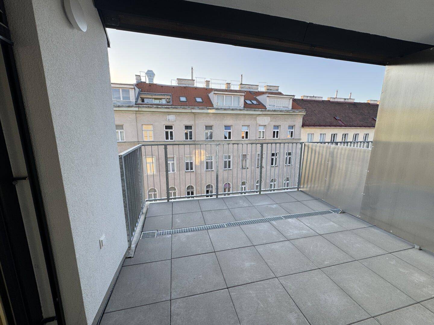 Geräumiger Balkon mit Fliesenboden und Blick auf die umliegenden Stadtgebäude.