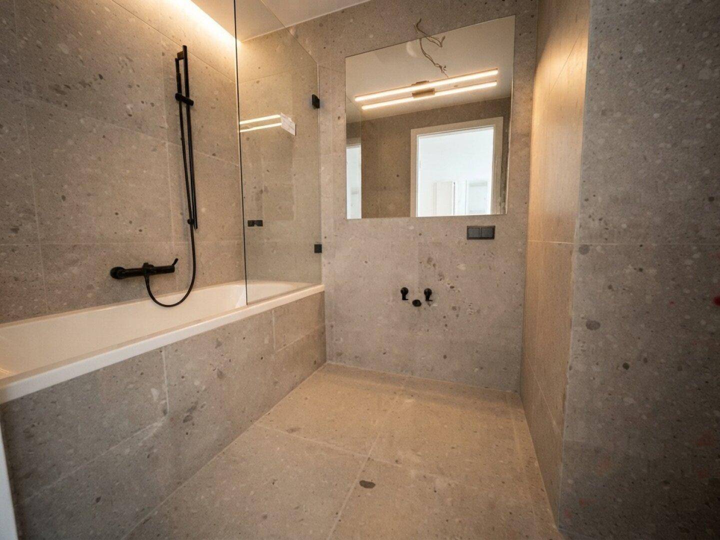 Modernes Badezimmer mit grauen Steinfliesen, integrierter Badewanne und Duschbereich.
