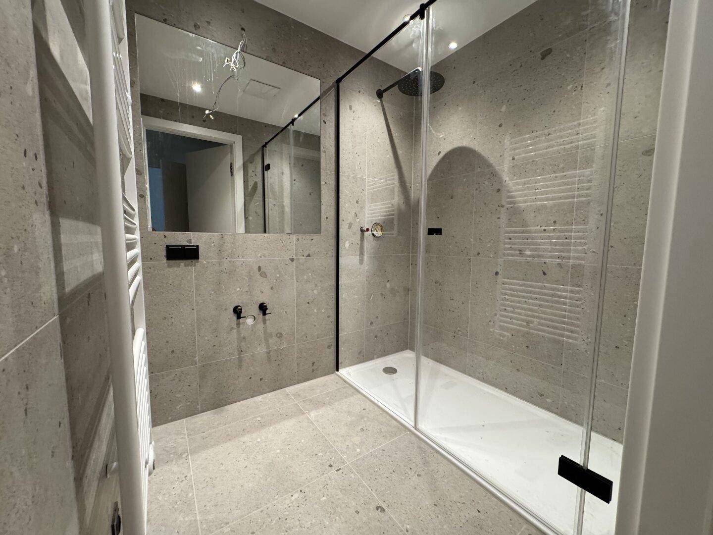 Modernes Badezimmer mit großer begehbarer Dusche und grauen Fliesen.