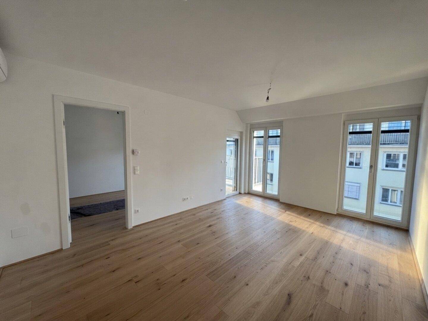 Lichtdurchfluteter Raum mit Holzboden und Zugang zu einem Balkon.