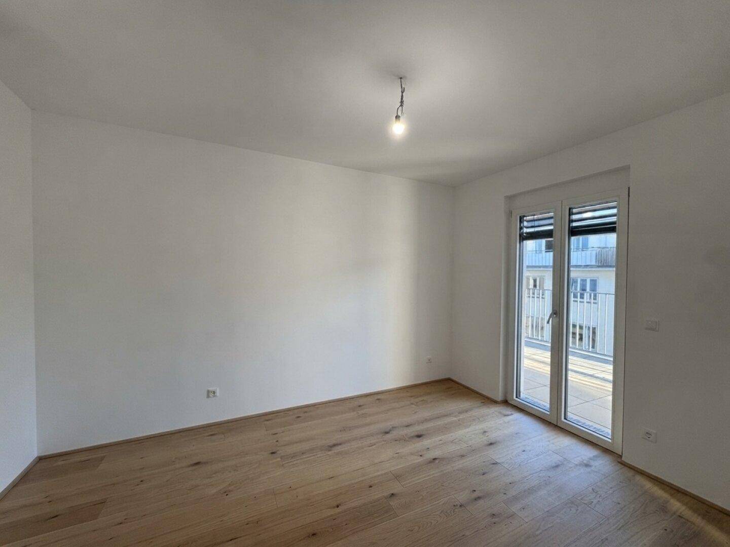 Helles Schlafzimmer mit Holzboden und Zugang zu einem französischen Balkon.