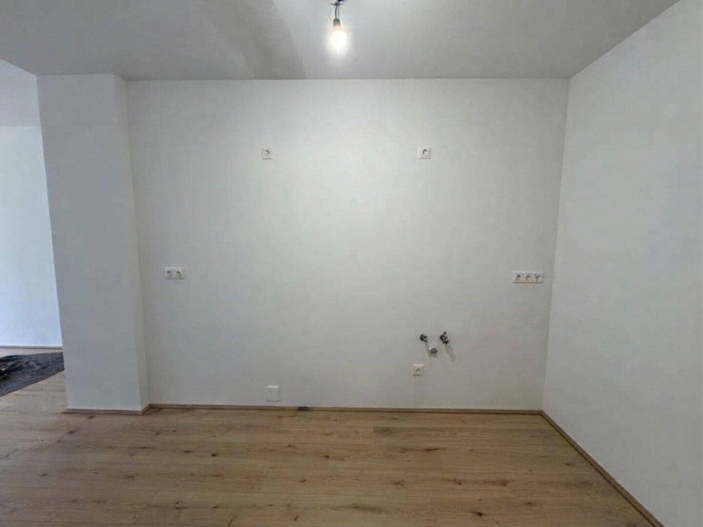 Leerer Küchenbereich mit Anschlüssen für eine Einbauküche und Holzboden.