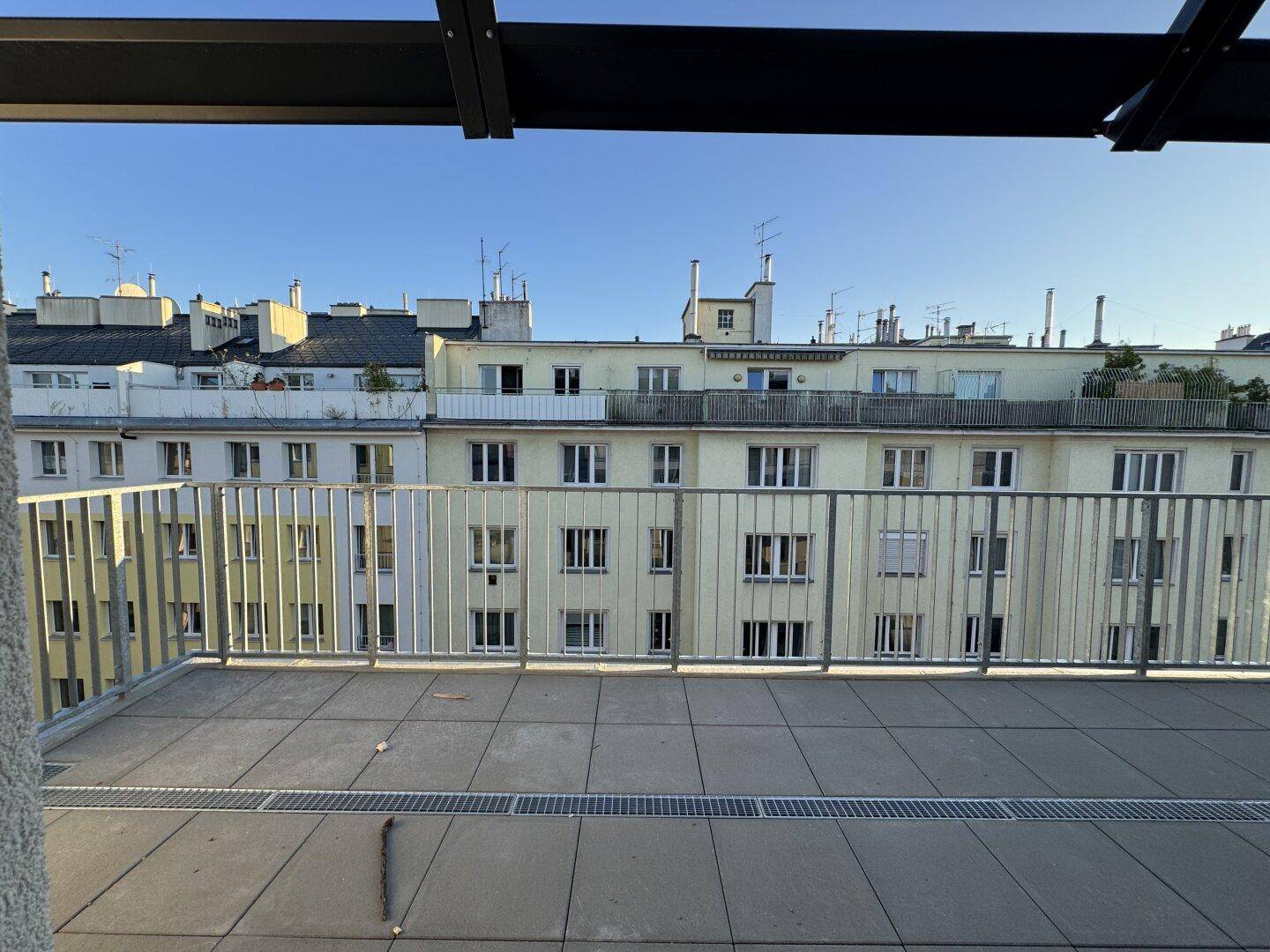 Geräumige Terrasse mit Blick auf die umliegenden Gebäude und den blauen Himmel.