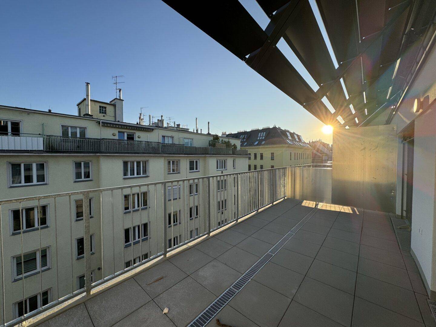 Sonniger Balkon mit weitem Blick über die Stadt und die umliegenden Dächer bei Sonnenuntergang.