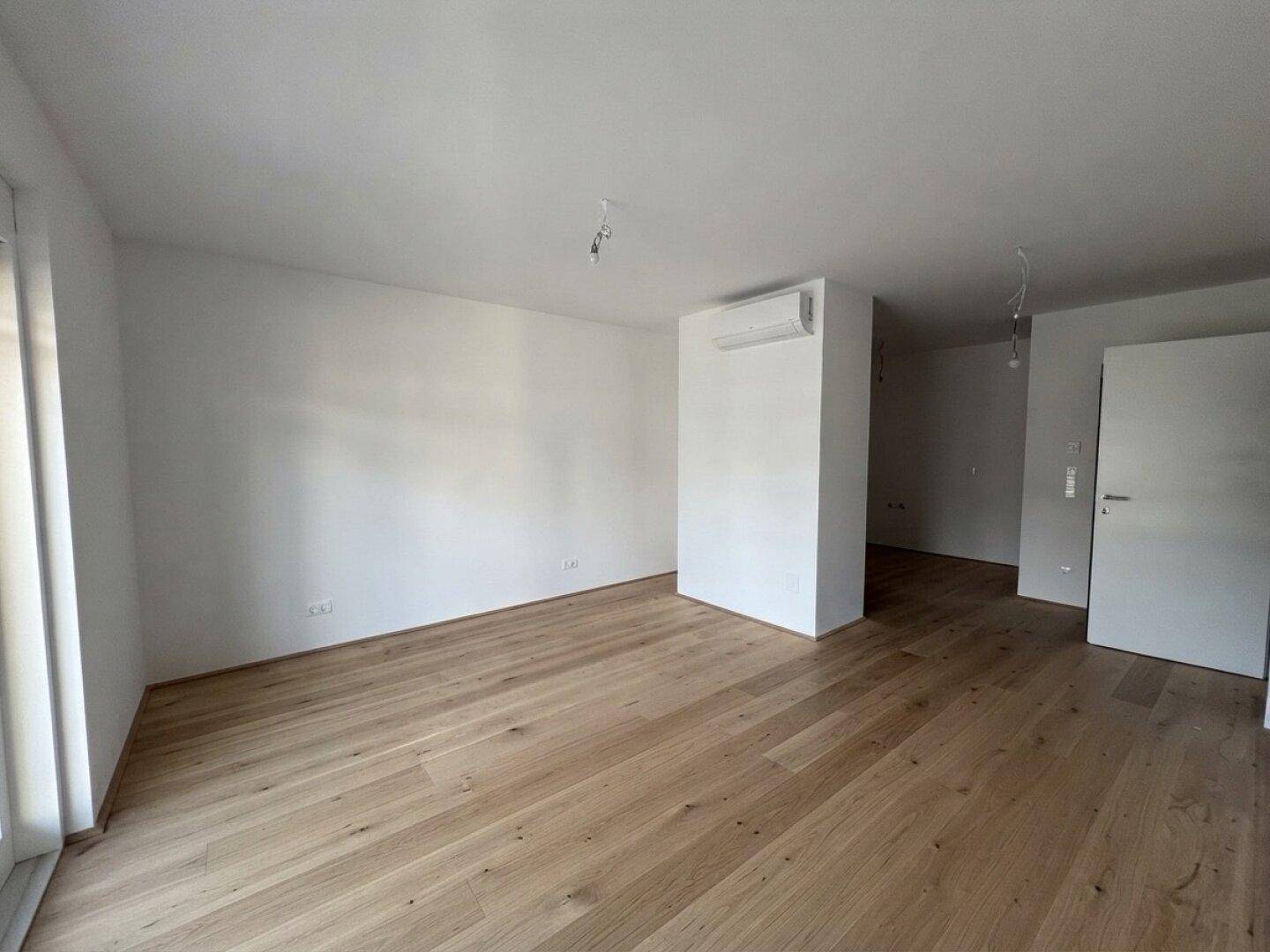 Geräumiger, heller Wohnbereich mit Holzboden und Klimaanlage, bereit zur Einrichtung.
