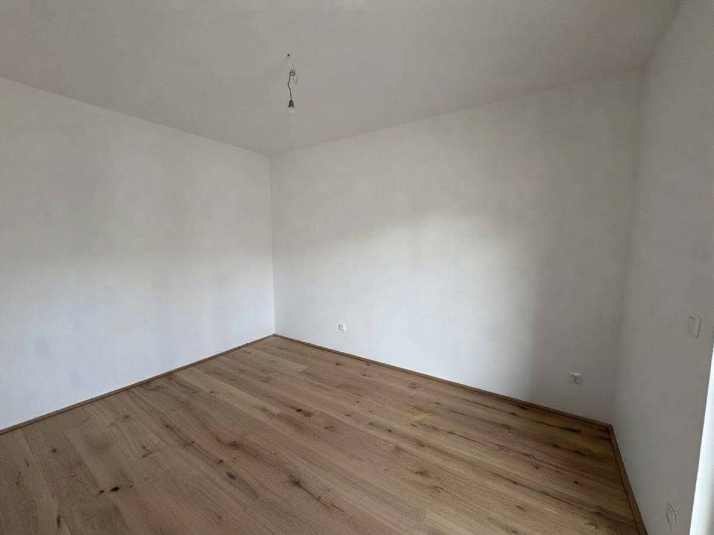Heller, leerer Raum mit Holzboden und weißen Wänden, ideal für ein Schlafzimmer oder Büro.