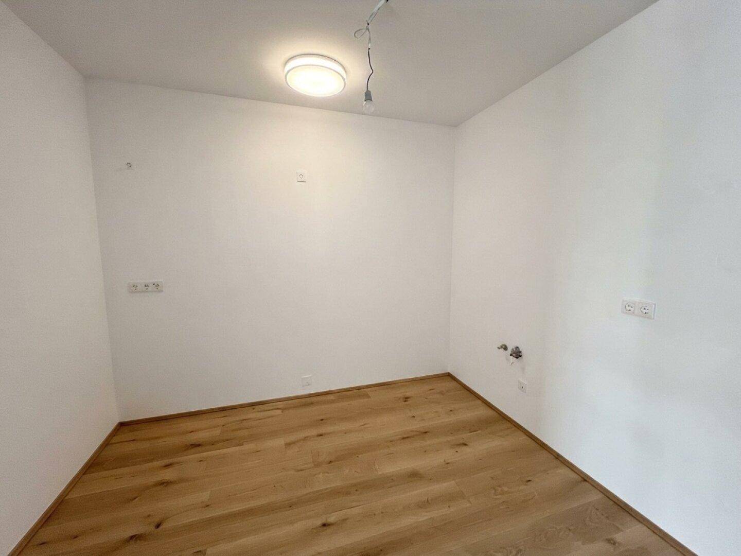 Leerer Raum mit hellem Holzboden und weißen Wänden, bereit für individuelle Gestaltung.