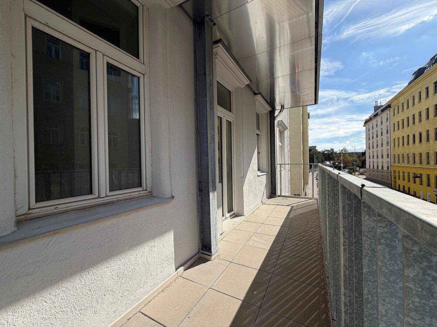 Langer Balkon mit Fliesenboden und weitem Blick über die städtische Umgebung.