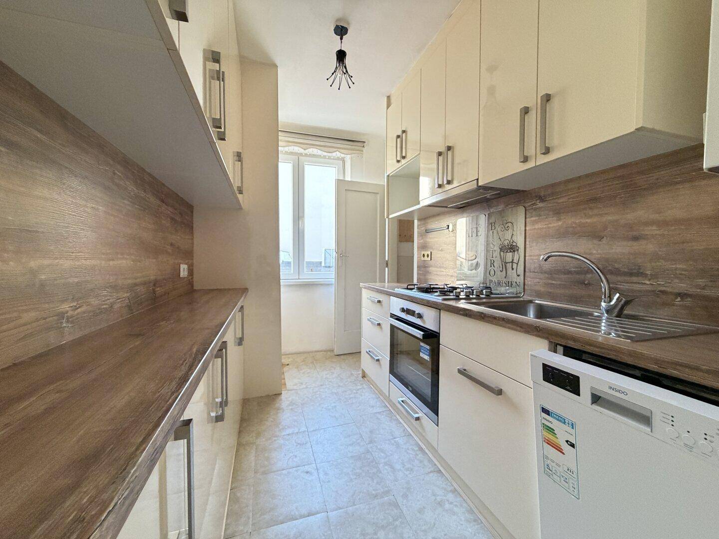 Moderne Küche mit hellen Schränken, Holzoptik-Arbeitsplatten und integrierten Geräten.