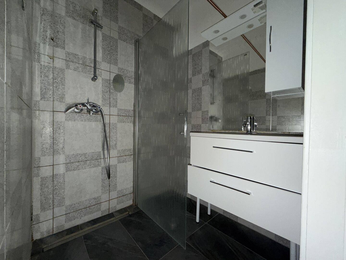 Badezimmer mit Duschkabine, Waschbeckenunterschrank und grauen Fliesen.