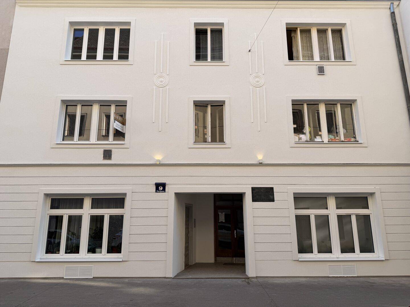 Die frisch renovierte Fassade eines Mehrfamilienhauses mit mehreren Fenstern und Eingangsbereich.