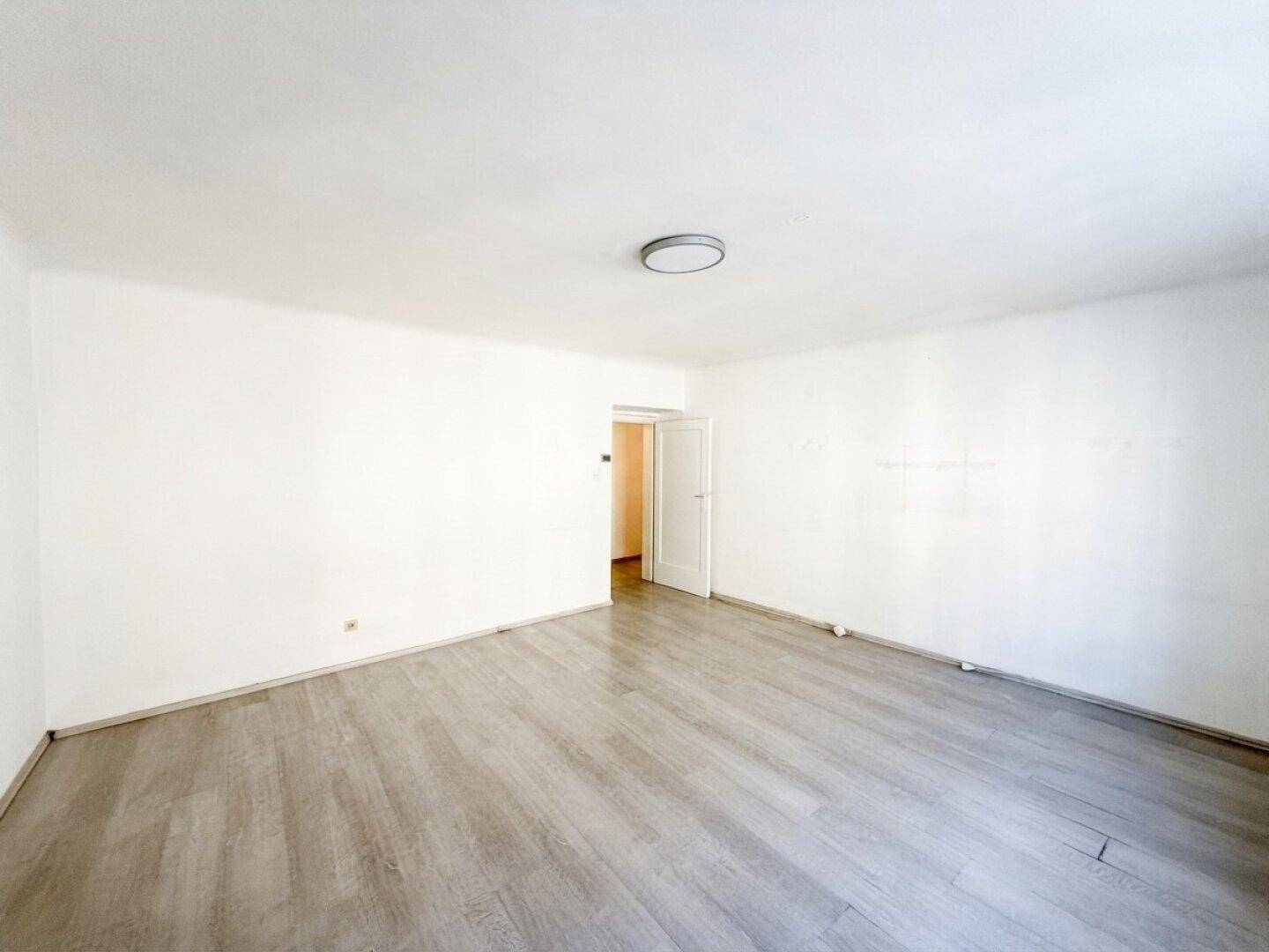 Leeres, helles Wohnzimmer mit modernem Laminatboden und weiß gestrichenen Wänden.