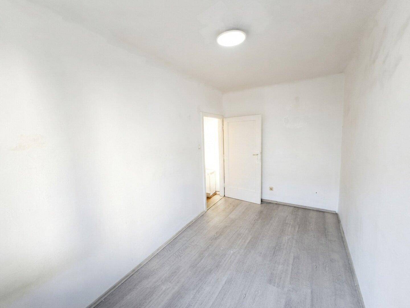 Helles, leeres Schlafzimmer mit Laminatboden und weiß gestrichenen Wänden.