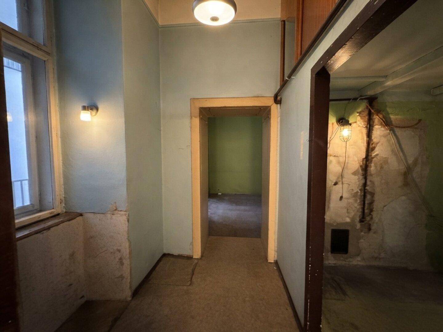 Alter Flur mit abgenutzten Wänden und Blick in einen weiteren Raum, der renoviert werden muss.