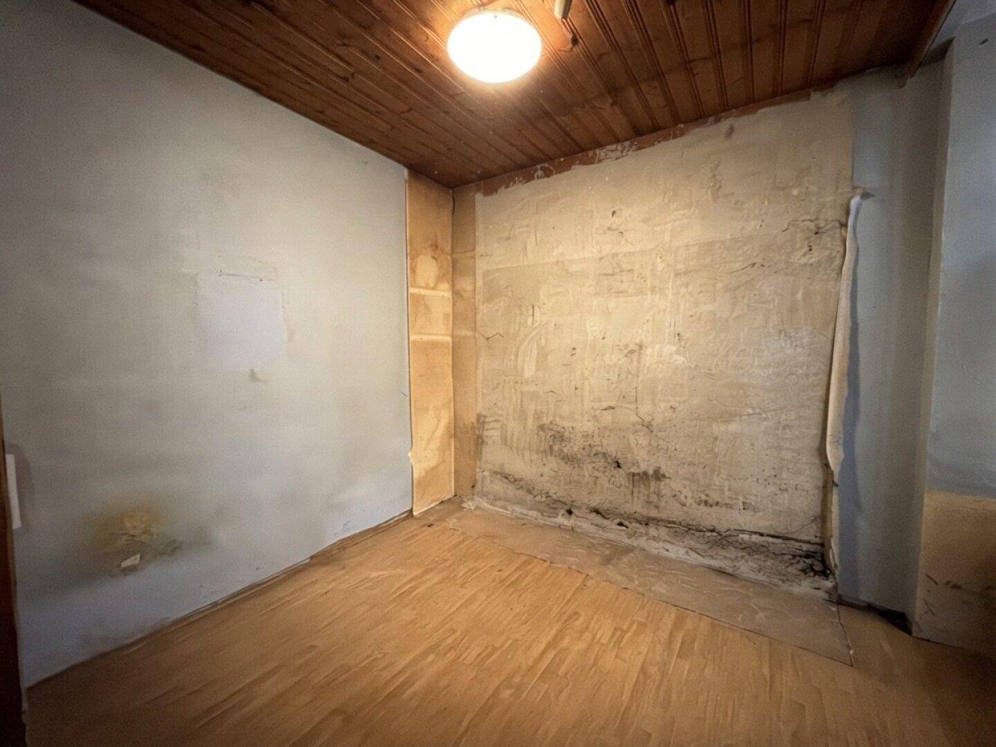 Kleiner Raum mit Holzdecke und abgenutzten Wänden, bereit zur umfassenden Renovierung.