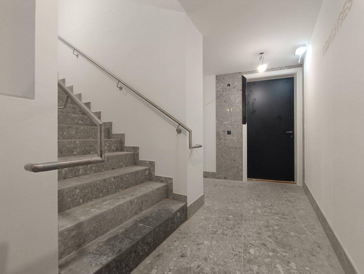 Treppenhaus mit modernem Geländer und grauen Fliesen im gesamten Bereich.