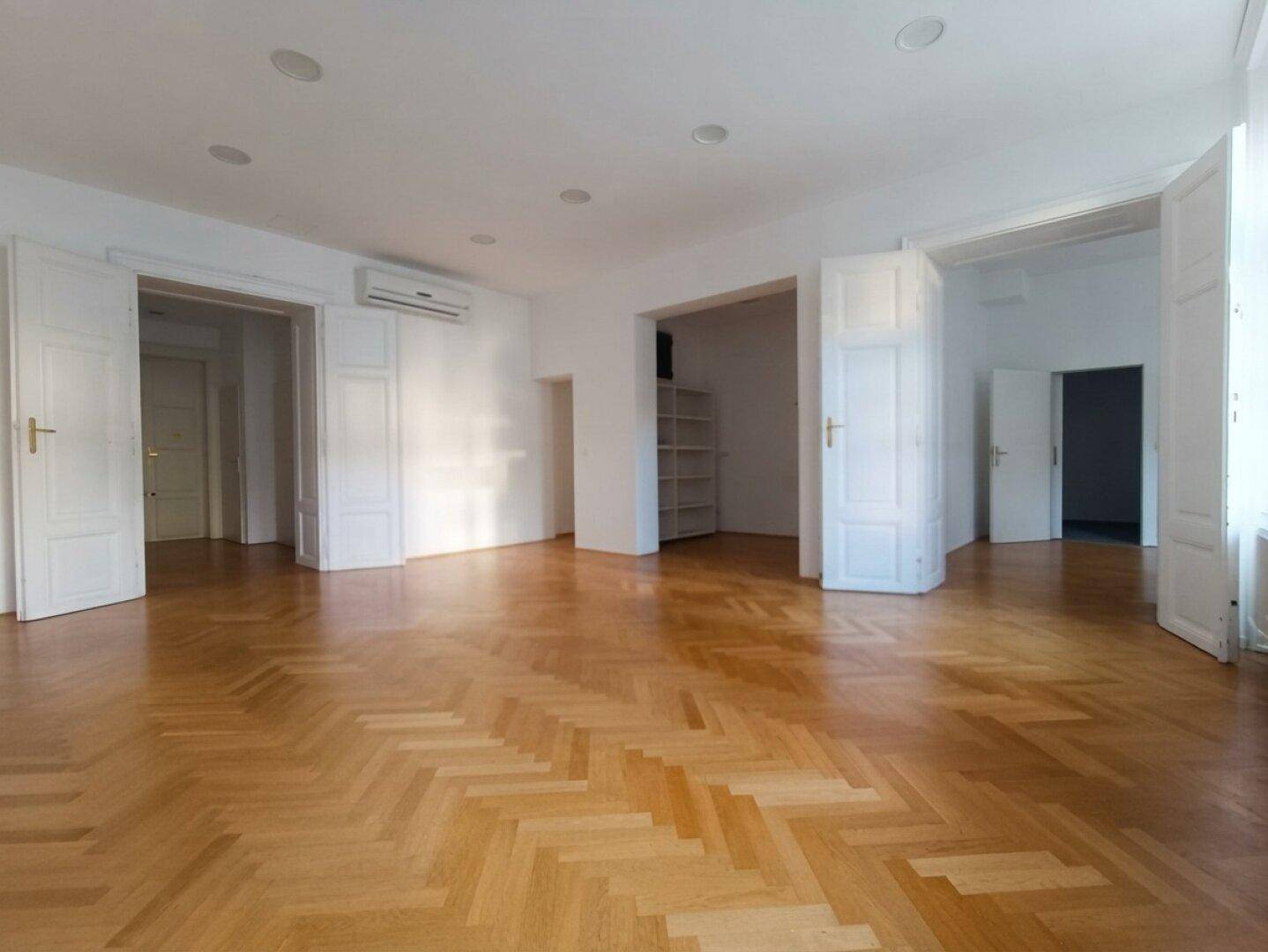Geräumiges Wohnzimmer mit klassischem Fischgrätparkett und vielen Türen, das viel Potenzial bietet.