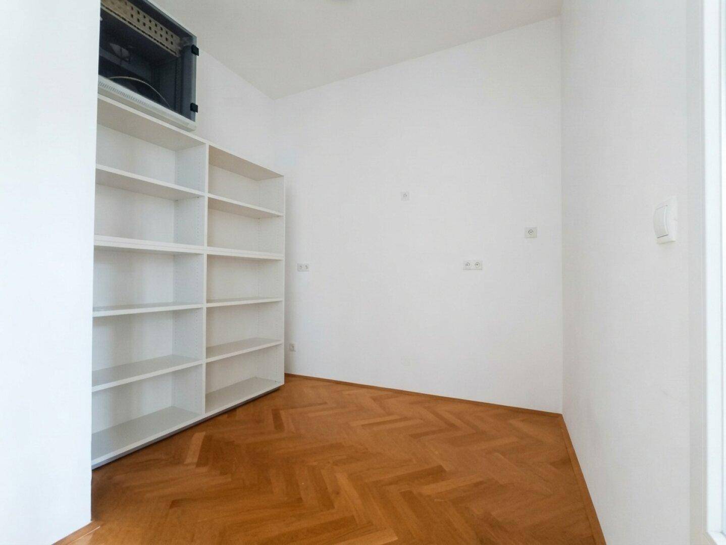 Praktischer Abstellraum mit eingebauten Regalen und Fischgrätparkett für zusätzlichen Stauraum.