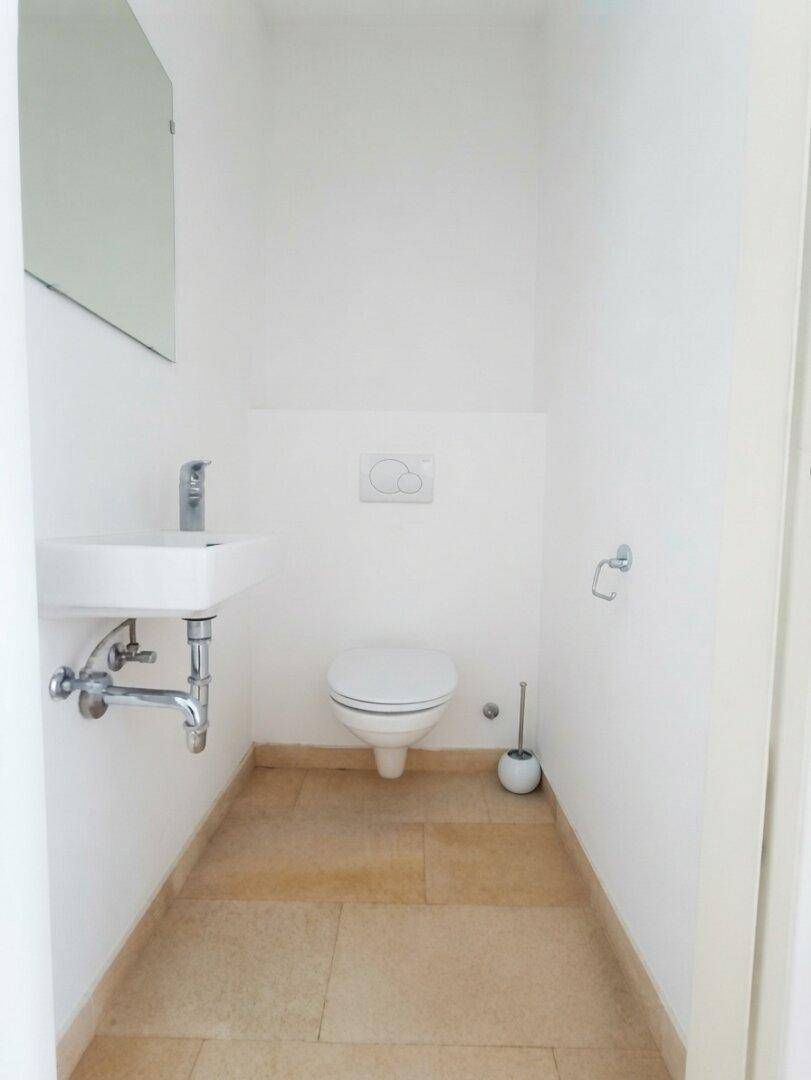 Kleines Gäste-WC mit Wand-WC, Waschbecken und hellen Fliesen, in modernem Design gehalten.
