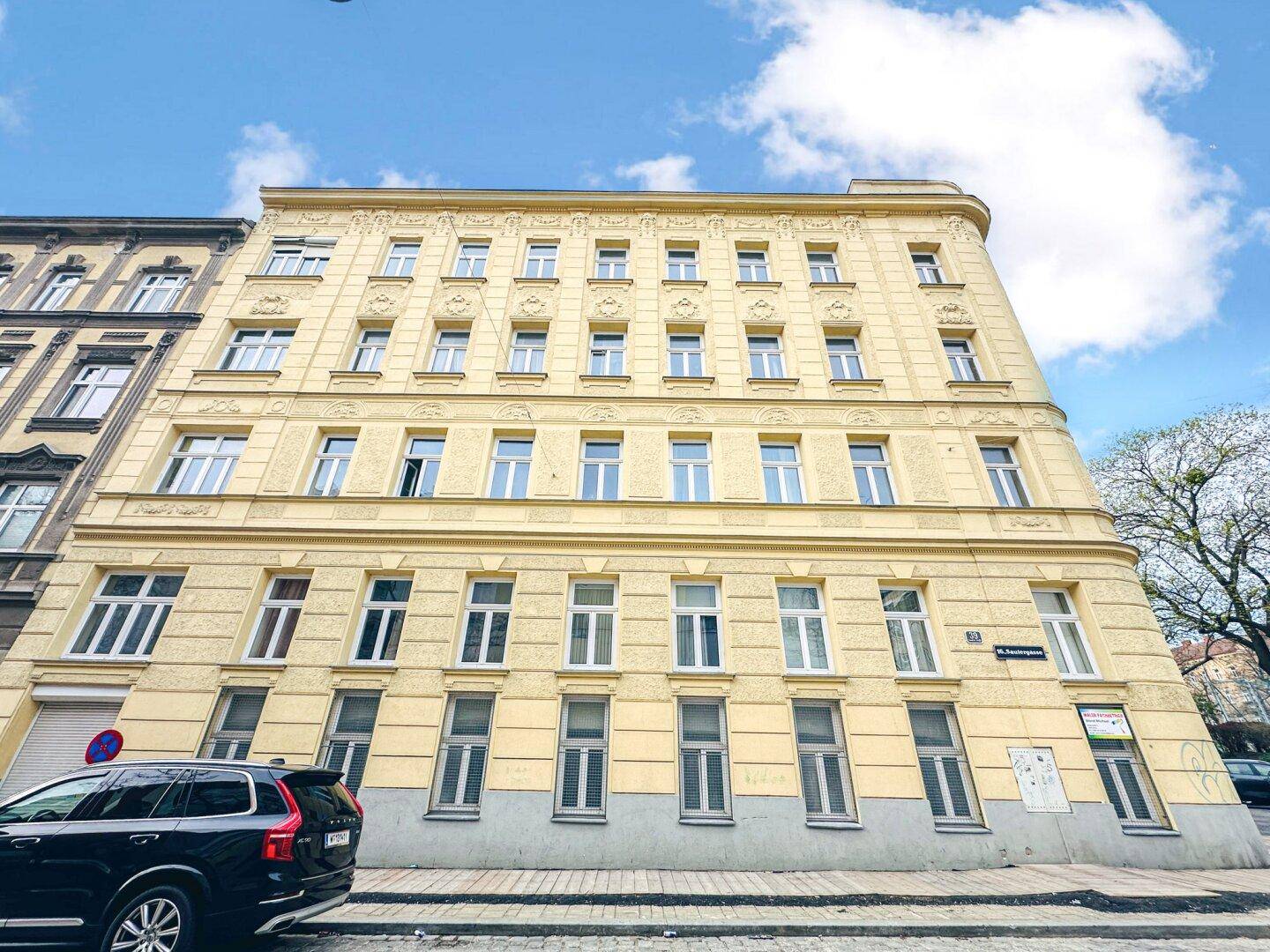 Klassisches Mehrfamilienhaus mit gelber Fassade und vielen Fenstern an einer städtischen Straße.