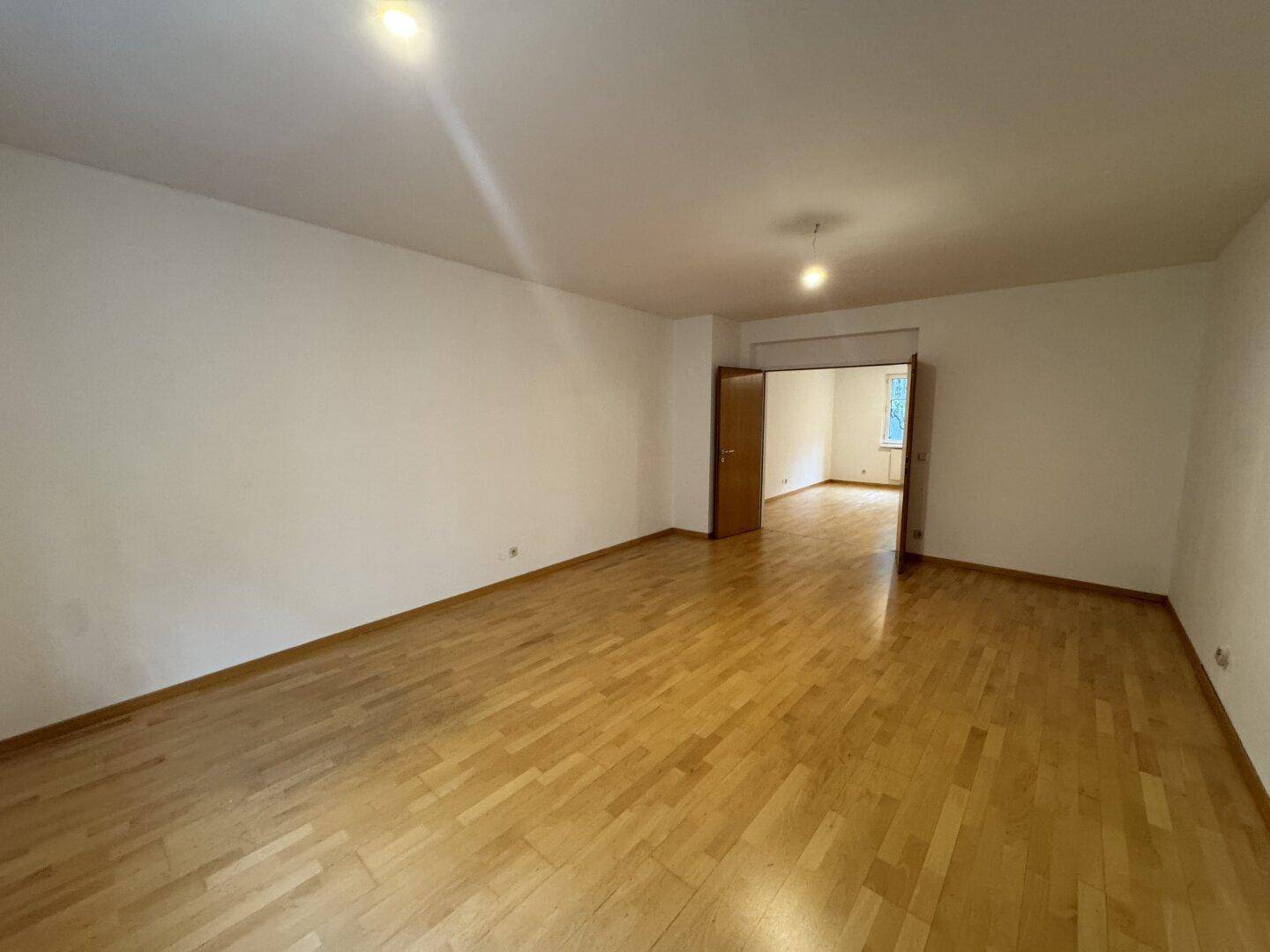 Großzügiger Wohnraum mit Parkettboden und offenem Durchgang zu einem angrenzenden Zimmer.
