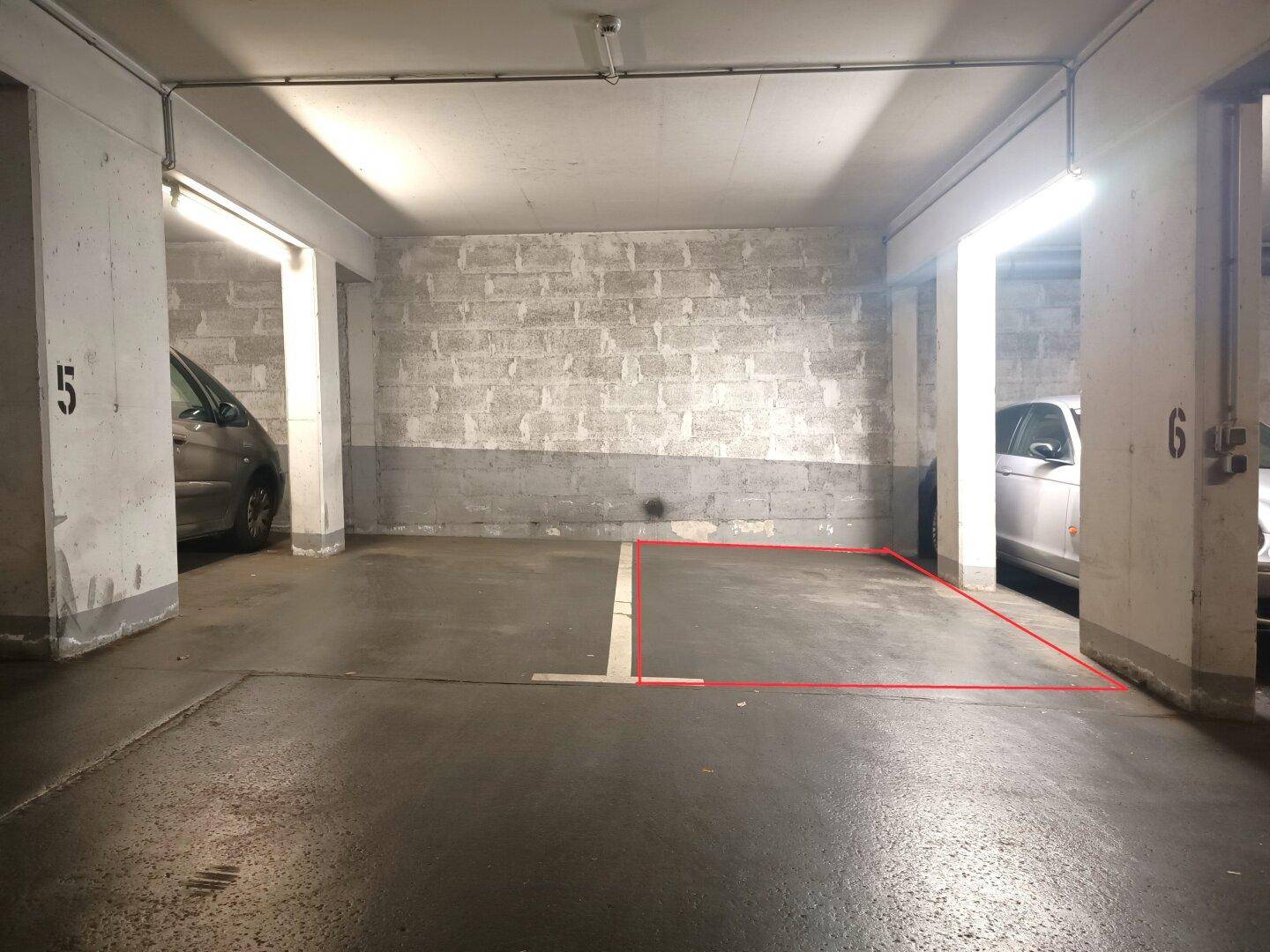 Leerer Parkplatz in einer Tiefgarage mit Betonwänden und hellen Leuchtstofflampen.