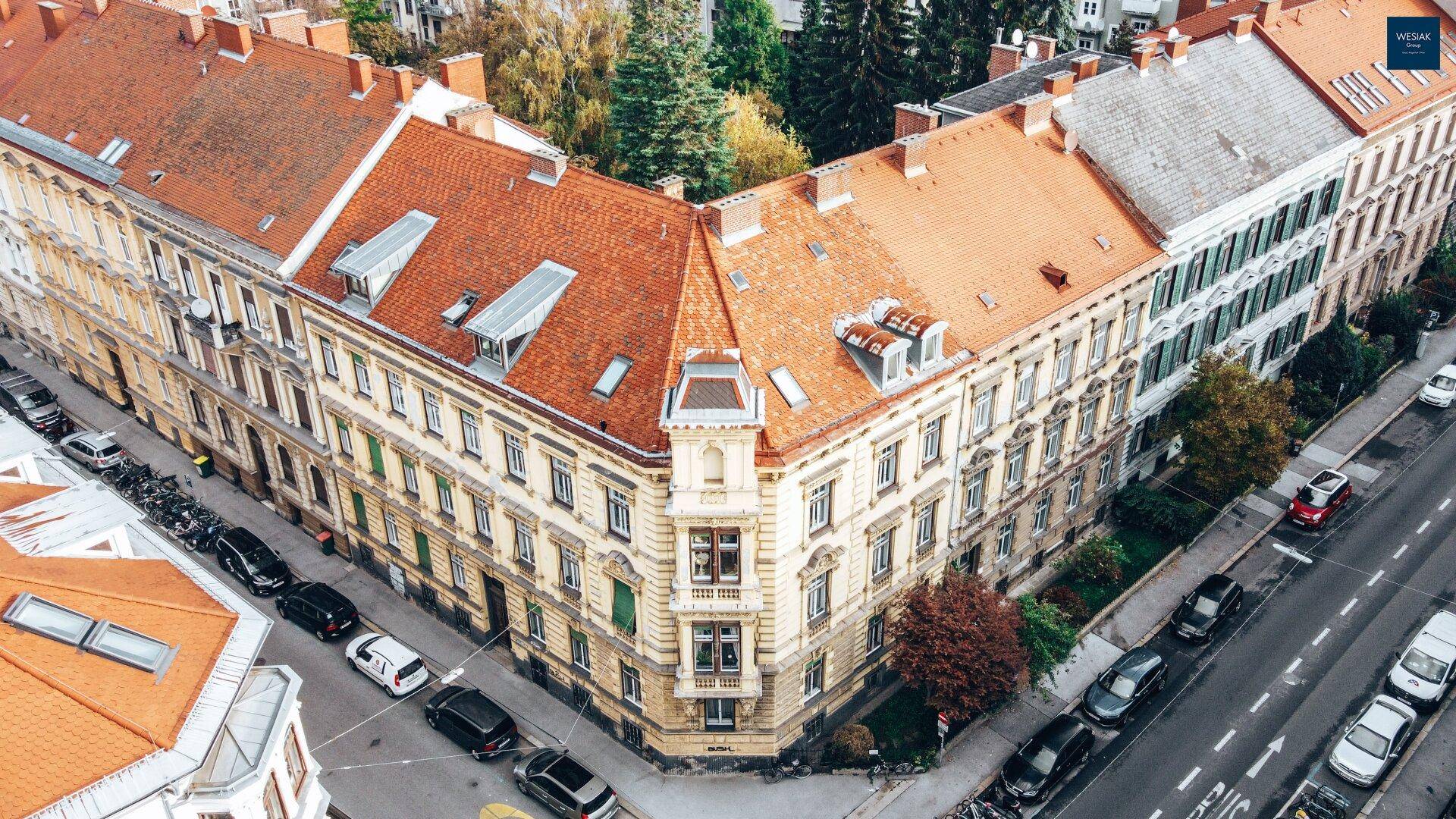 Historisches Eckgebäude mit traditionellem Ziegeldach und umliegender Stadtlandschaft aus der Vogelperspektive.