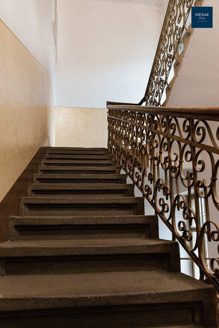 Historisches Treppenhaus mit kunstvollem schmiedeeisernem Geländer und Steinstufen.