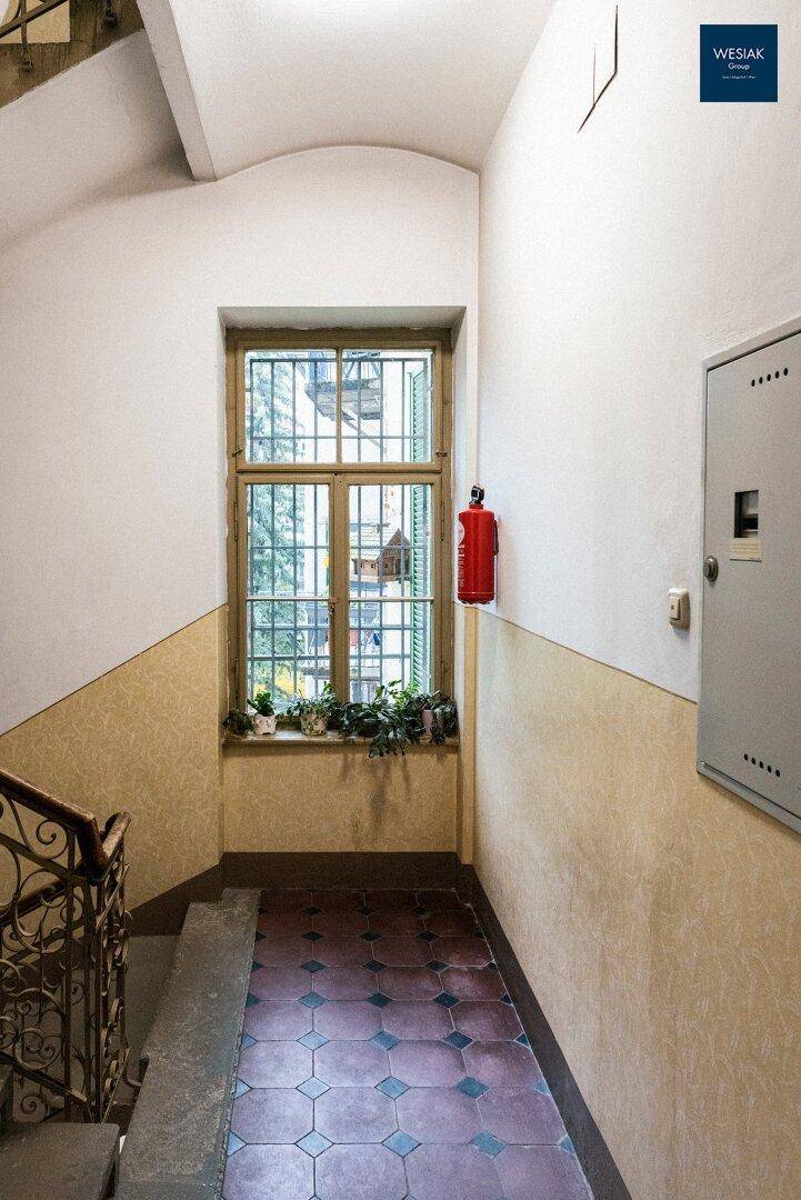 Heller Treppenabsatz mit Fenster, Gitter und traditionellen Fliesen auf dem Boden.