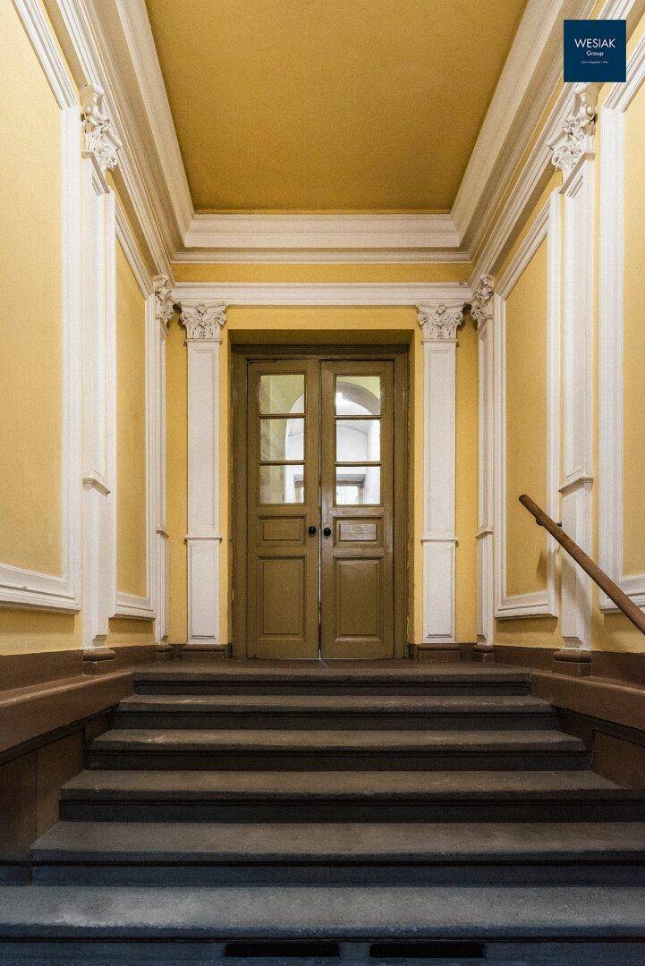 Eingangsbereich mit hohen Decken, Stuckverzierungen und einer imposanten Doppeltür.