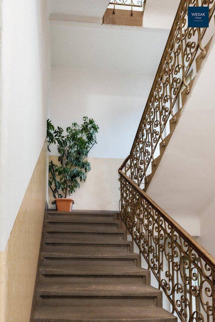 Historisches Treppenhaus mit schmiedeeisernem Geländer und einer dekorativen Pflanze.