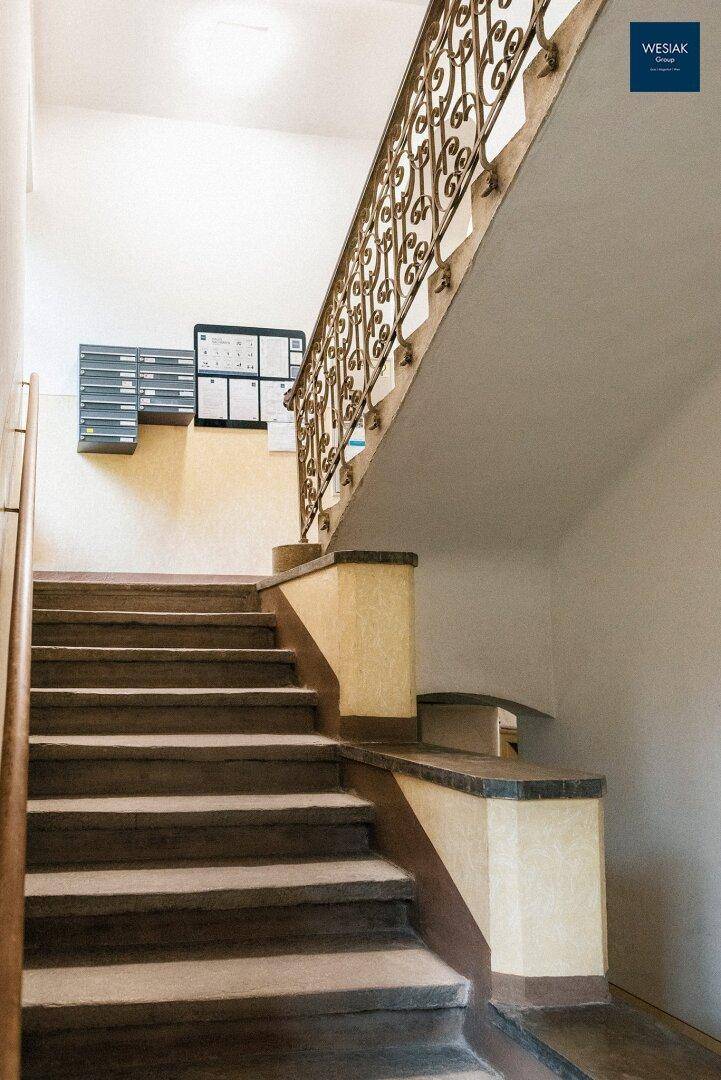 Treppenhaus mit schmiedeeisernem Geländer und Briefkästen an der Wand.
