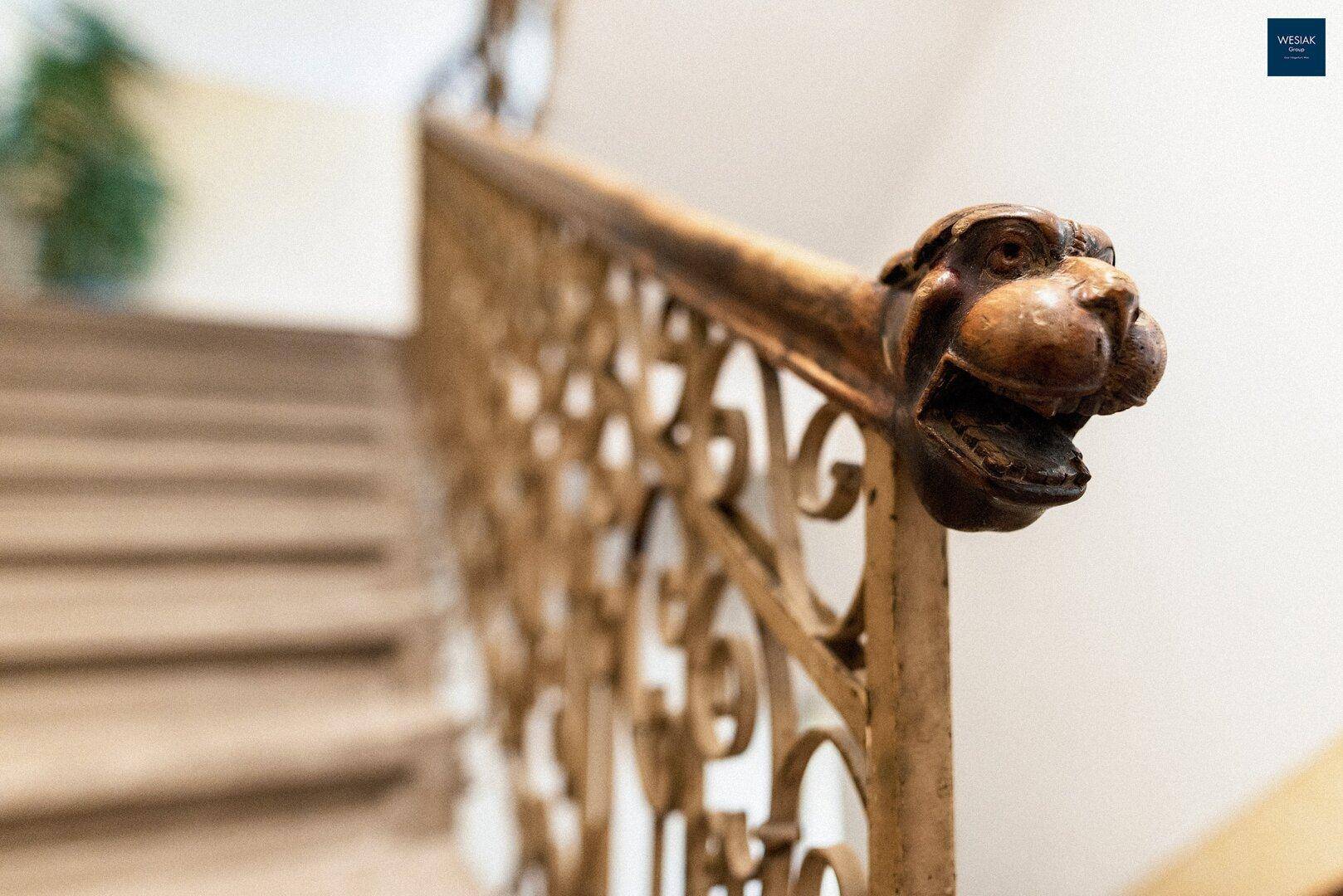 Detailaufnahme des kunstvollen Treppengeländers mit einer dekorativen Tierkopfverzierung.