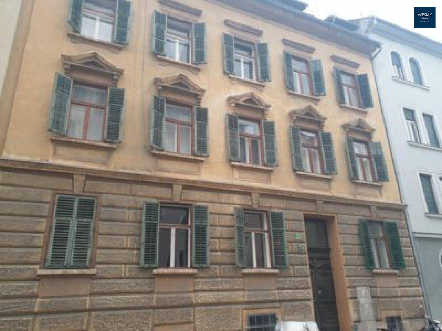 Historische Fassade eines Altbaus mit grünen Fensterläden und dekorativen Fensterrahmen.
