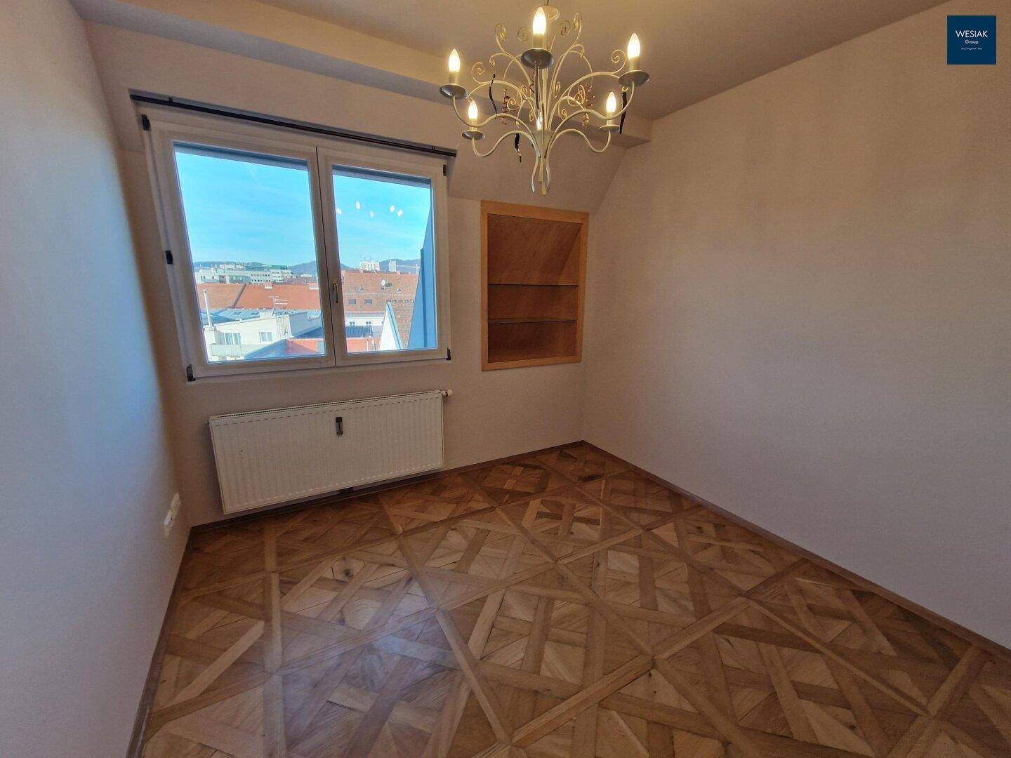 Helles Zimmer mit Parkettboden, großem Fenster und klassischem Kronleuchter.
