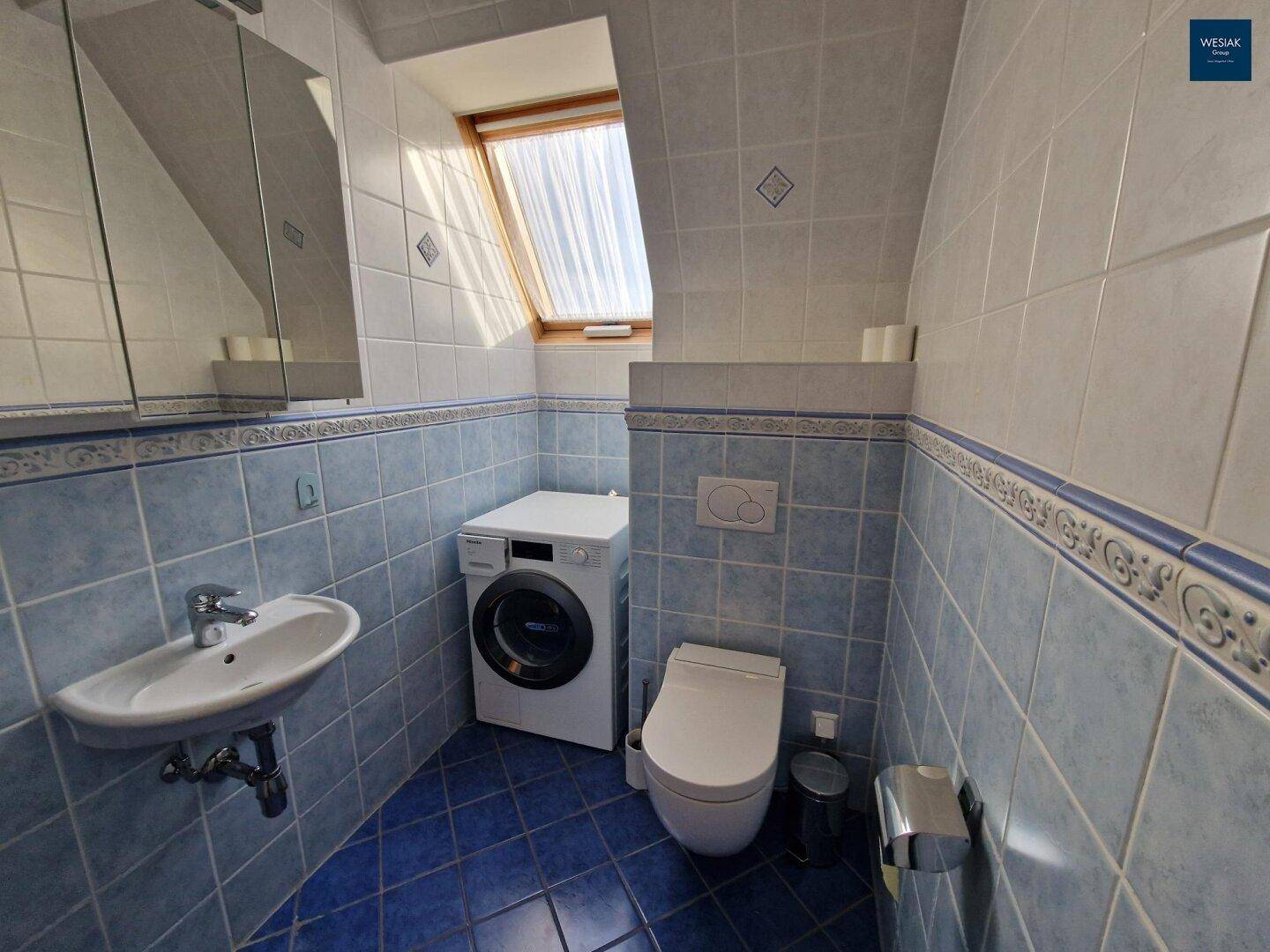 Kleines Badezimmer mit blauen Fliesen, WC, Waschbecken und Dachfenster.