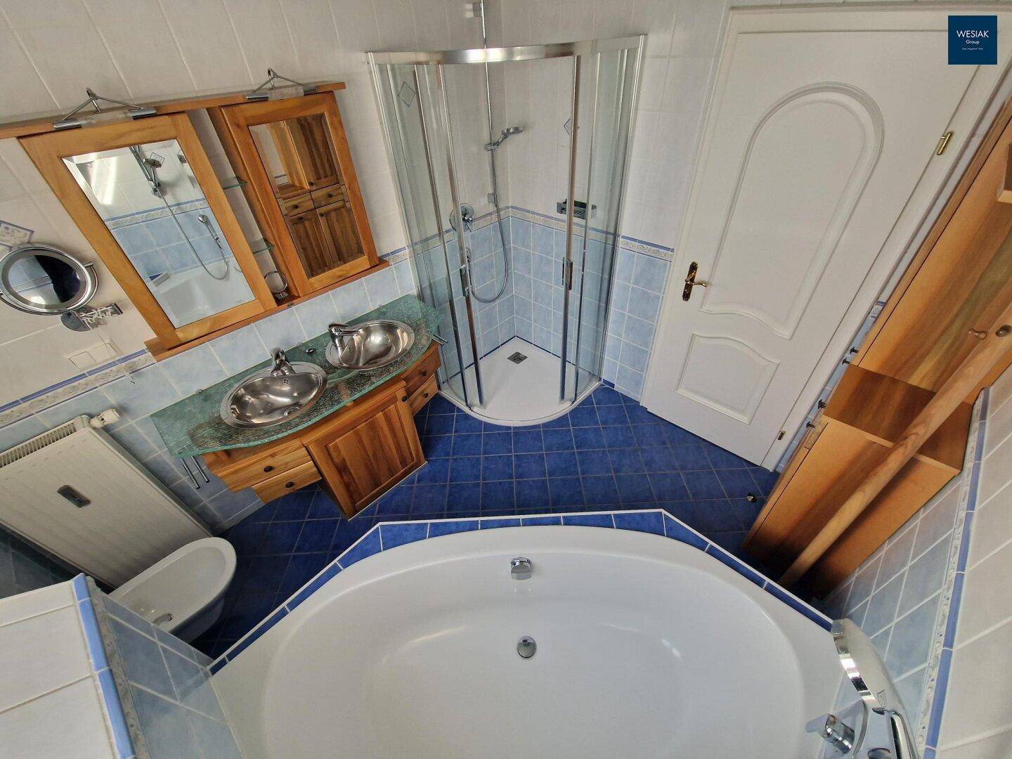 Badezimmer mit blauen Fliesen, Eckbadewanne, Duschkabine und Doppelwaschbecken.