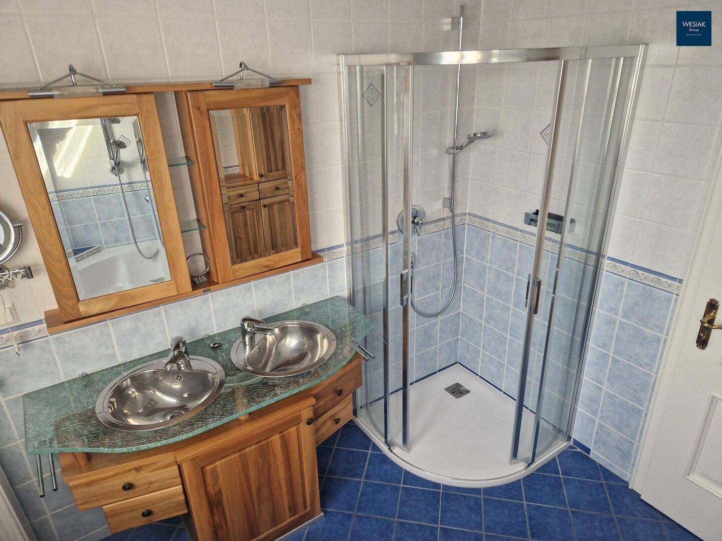 Badezimmer mit blauen Fliesen, Duschkabine und Doppelwaschbecken mit Holzunterschrank.