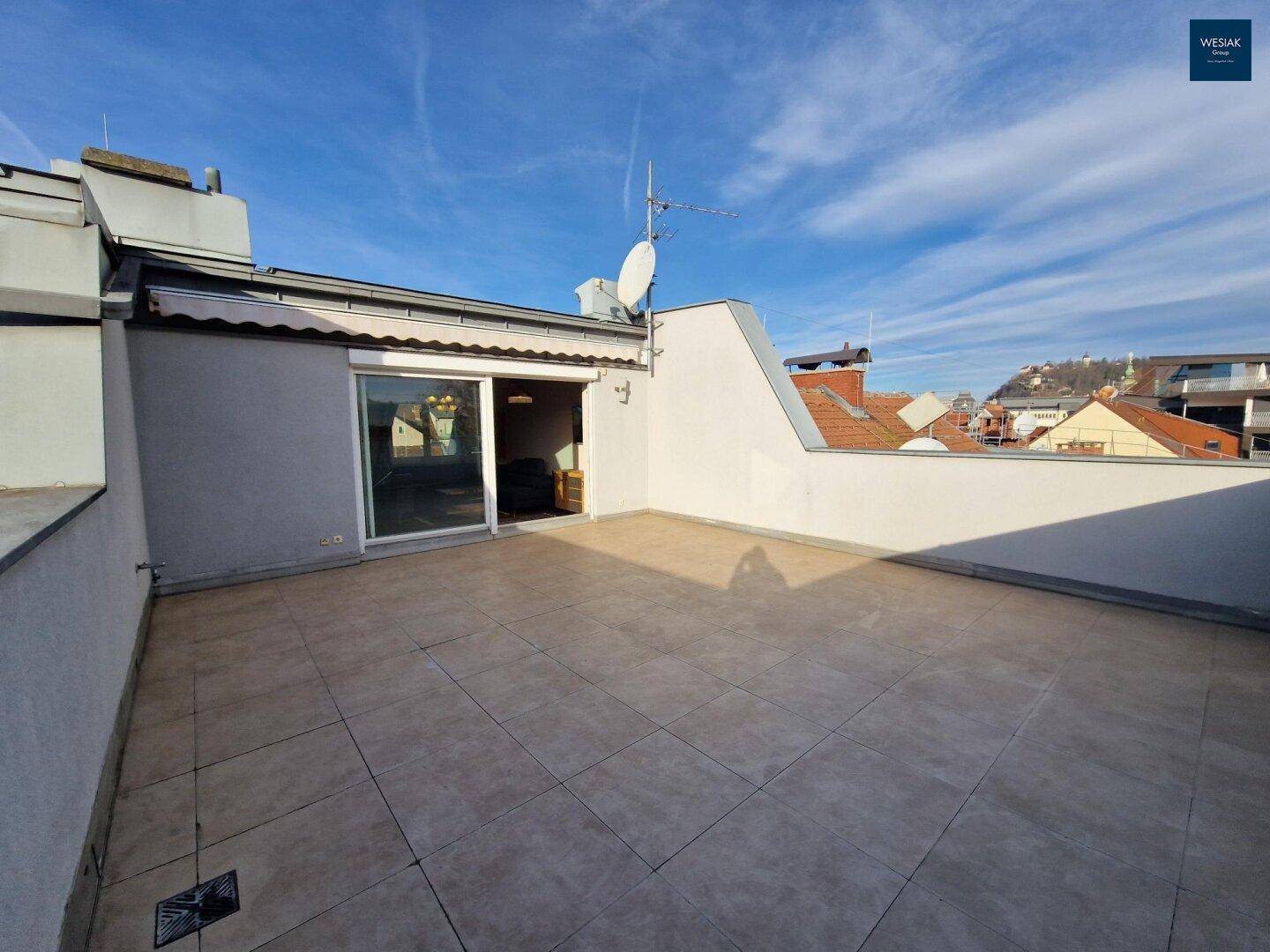 Geräumige Dachterrasse mit hellen Fliesen und Zugang zum Innenbereich.