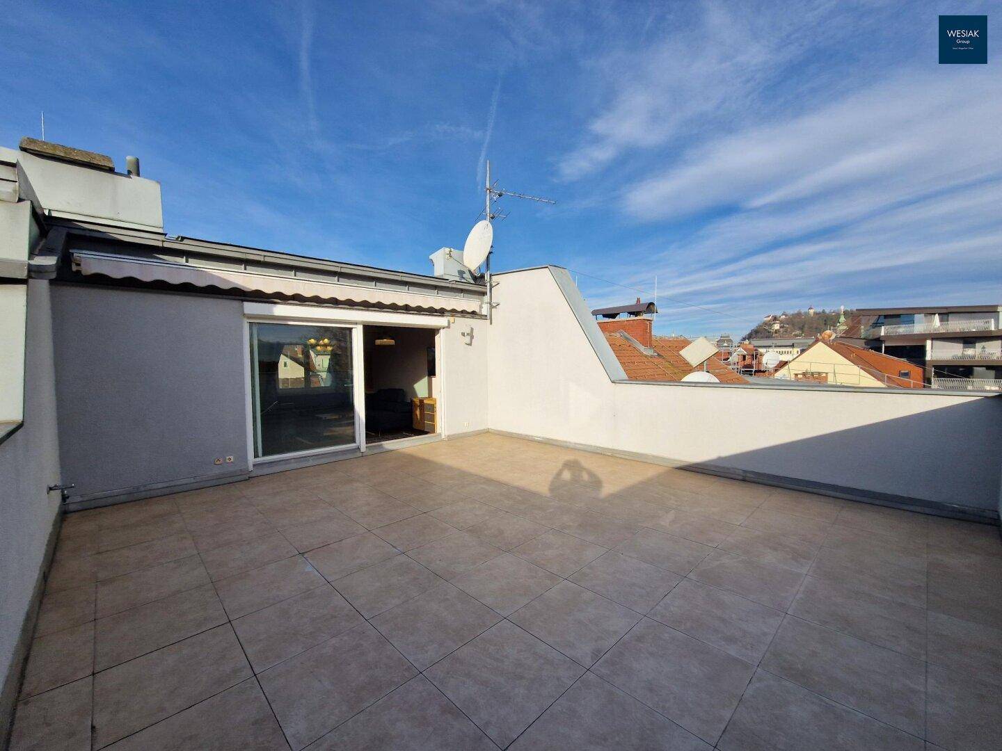 Helle Dachterrasse mit Fliesenboden und direktem Zugang zum Wohnbereich.