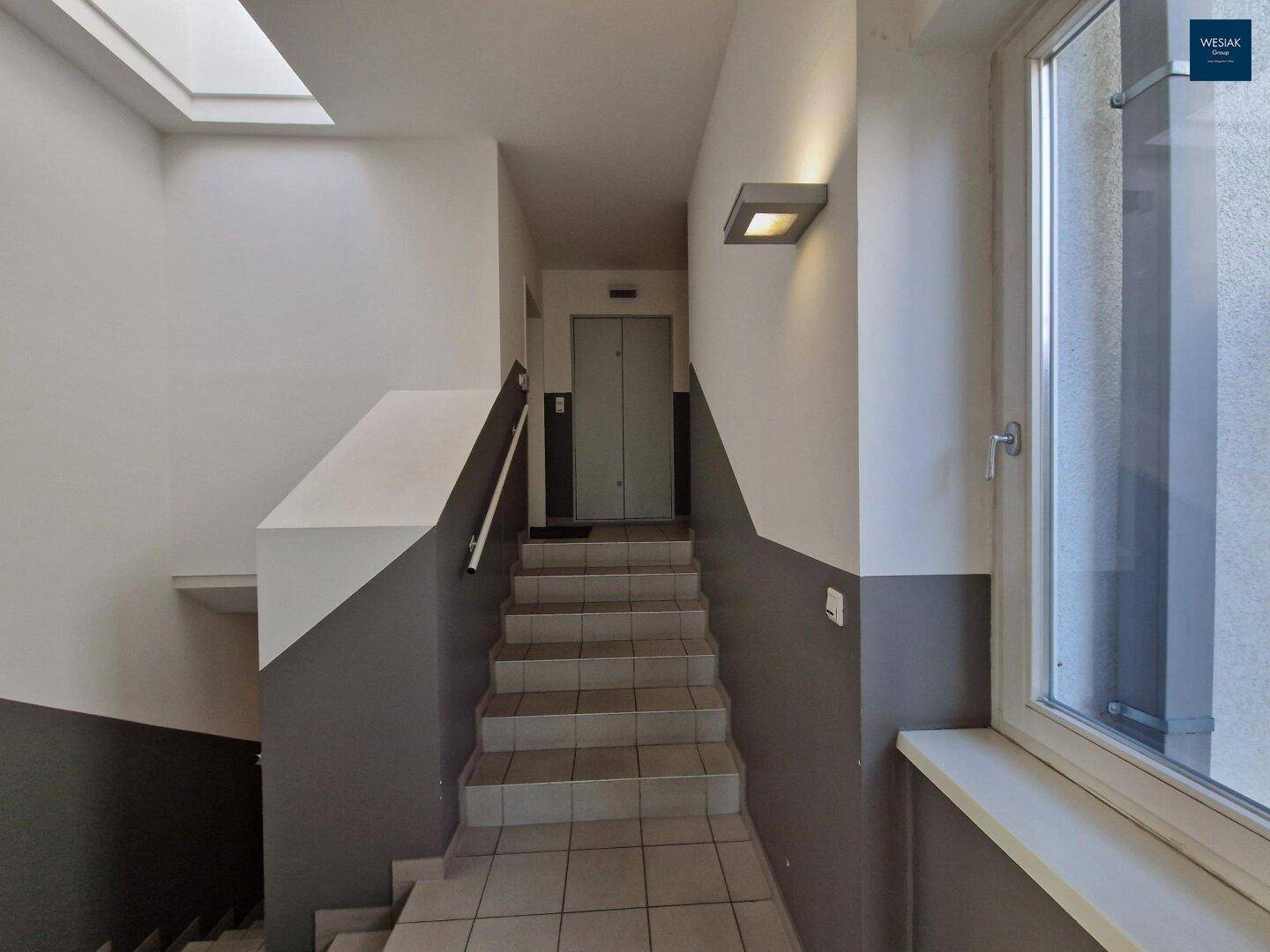 Treppenhaus mit Fliesenboden und Zugang zu einem modernen Aufzug.